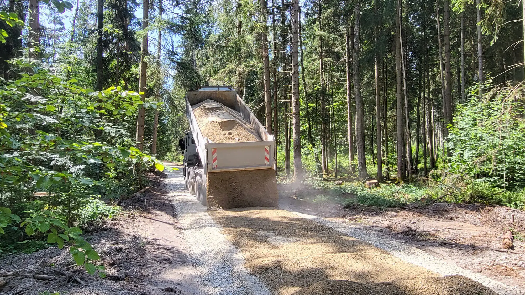 LKW kippt Schottermaterial auf Waldweg ab